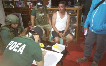 <p><strong>ARRESTED.</strong> Reelectionist Barangay Malasila Chairman Melvin Fontajada (in handcuffs) of Makilala, North Cotabato, looks on as anti-narcotics personnel record the illegal drugs seized from his house during a pre-dawn raid Wednesday (May 16). <em><strong>(Photo by DXND – Kidapawan)</strong></em></p>